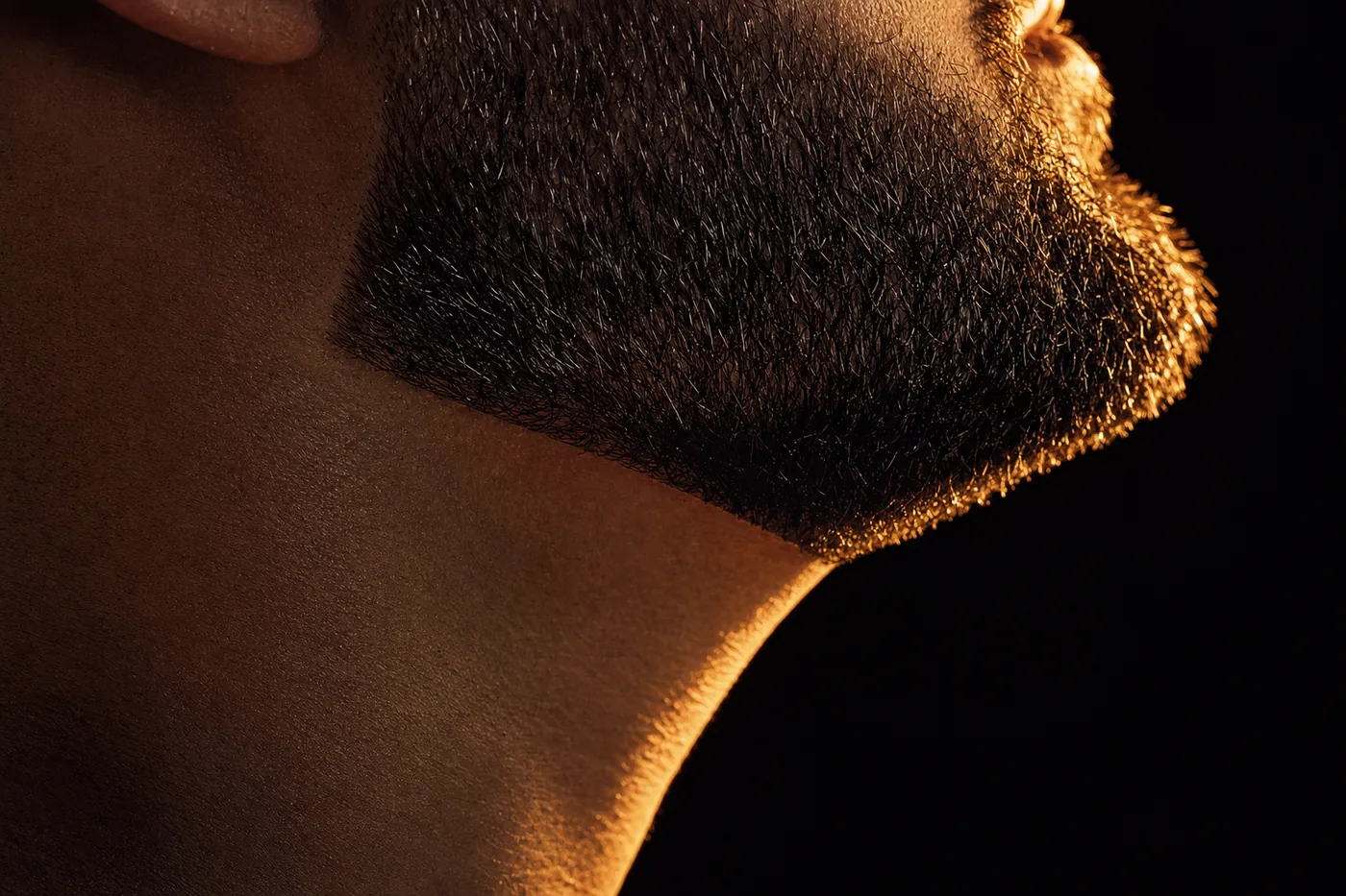 Close da linha da barba no maxilar, com a transição marcada pela luz